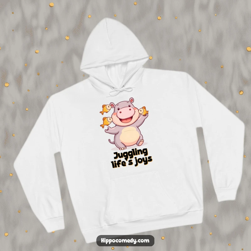 Funny happy hippo hoodie featuring a smiling hippopotamus juggling three small fish, embodying joy, skill, and cozy comfort.