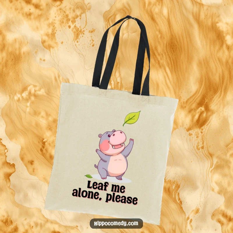 Funny tote bag featuring a determined hippopotamus humorously trying to catch a falling leaf, ideal for carrying items.